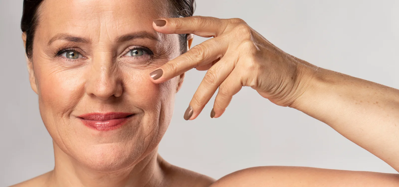 Ältere Dame mit leichten Falten im Gesicht posiert mit Fingern am Auge